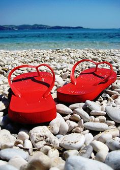 two red flip flops sitting on top of a rocky beach next to the ocean