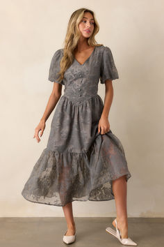 Adorn yourself in the enchanting beauty of our Faded Blossoms Grey Floral Puff Sleeve Midi Dress. Comfortable and stylish with puff sleeves and a flowy silhouette, this dress is perfect for any occasion. The subtle floral print adds a touch of elegance, making you feel confident and beautiful. This grey floral dress features a v-neckline, faux corset waist with button detailing, a flowy skirt with a slightly sheer bottom tier, and short puff sleeves. Grey Floral Dress, Puff Sleeve Midi Dress, Corset Waist, Dress Comfortable, China Design, Sleeve Midi Dress, Flowy Skirt, Grey Floral, Feel Confident