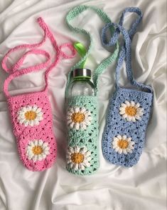 three crocheted water bottles are laying on a white sheet and one has a green bottle in it