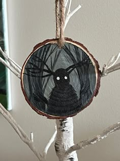 a black cat hanging from a tree with branches in the foreground and a mirror behind it