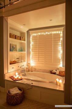 a bathtub with candles lit up in front of the tub and shelves behind it