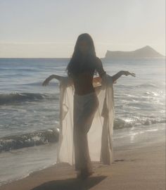 a woman standing on top of a sandy beach next to the ocean with her arms outstretched