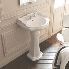 a white pedestal sink in a bathroom next to a mirror and towel on the floor