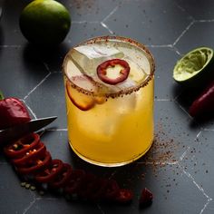 a glass with some fruit on it next to limes and chili slices, including a knife