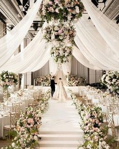 a bride and groom are standing under an archway decorated with white draping, pink flowers and greenery