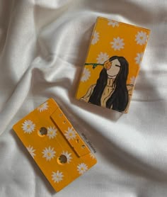 an orange cassette with a painting of a woman holding a flower in her mouth on top of a white sheet