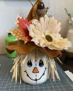 a ceramic pumpkin with a scarecrow's hat and flowers on it sitting on a table