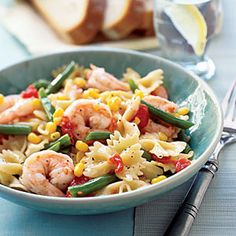 a bowl filled with pasta and shrimp on top of a table next to silverware