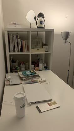 a white desk topped with books and a cup of coffee next to a book shelf