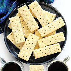 some crackers are on a black plate with two cups of coffee next to them