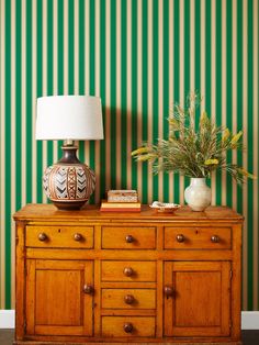 a lamp on top of a dresser next to a green striped wall