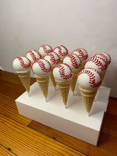 six cones with red and white baseballs on them sitting on a wooden floor next to a wall