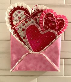 a pink envelope with hearts on it hanging from the wall in front of a white brick wall