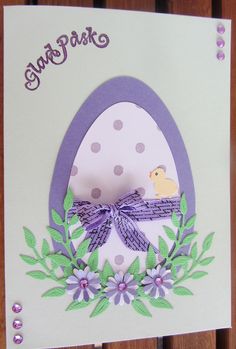 an easter card with a chick in the egg on it's side and purple ribbon