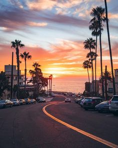 the sun is setting behind palm trees and cars parked on the side of the road