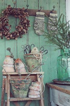 an old wooden table topped with potted plants next to a wreath and pine cones