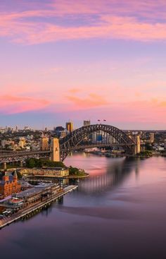 an aerial view of the sydney harbour bridge and opera house at sunset, with pink clouds in the sky