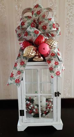 a small white lantern with a red ornament and bow on it's front