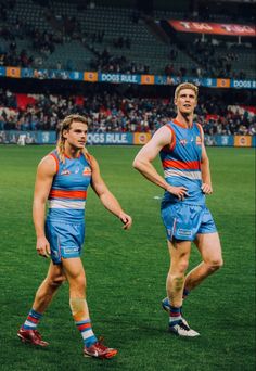 two men in blue and orange uniforms are walking on the field at a sporting event