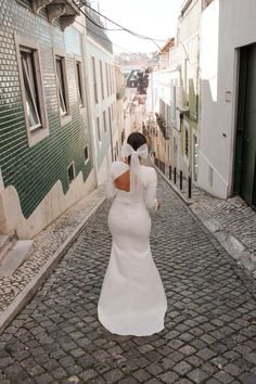 a woman in a white dress is walking down the cobblestone street with her back to the camera