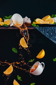 orange slices are falling into the water with tea cups and lemons in the background