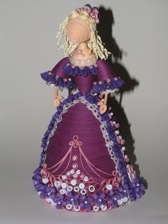 a figurine is dressed in purple and pink with flowers on the bottom half