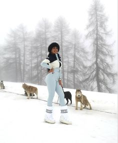 a woman standing in the snow with dogs behind her