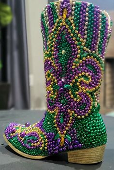 a pair of purple and green beaded boots on top of a gray surface with a plant in the background