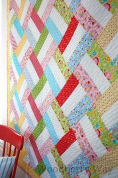 a colorful quilt is hanging on the wall next to a red chair and table with a striped pillow