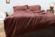 a bed with red sheets and pillows in a room next to a white chair on the floor