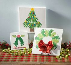 three christmas cards with handprints on them sitting on a table next to decorations