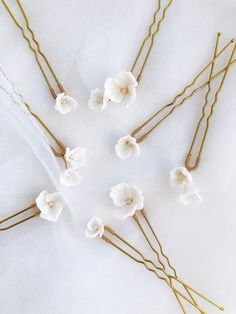 white flowers and gold bobby pins are arranged on a white cloth