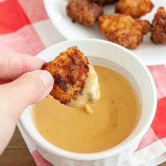 a person dipping cheese into a bowl of soup with tater tots on the side