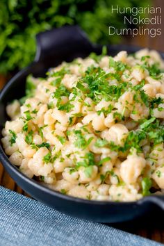 a bowl filled with macaroni and cheese on top of a wooden table next to parsley