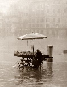 a person sitting under an umbrella in the water with food on a cart underneath it