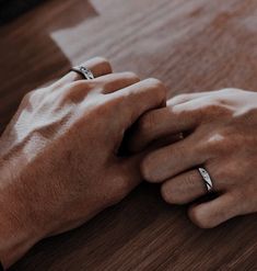 two hands holding each other on top of a wooden table with their wedding bands wrapped around them