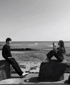 two people are sitting on rocks near the ocean and one is holding a cell phone