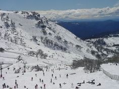 a group of people skiing down a snow covered mountain side with mountains in the background