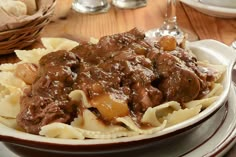 a plate full of pasta and meat with gravy on the table next to bread