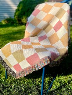 an orange and white checkered blanket sitting on top of a metal chair in the grass