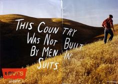 a man standing on top of a grass covered hill next to a sign that says, this country was not built by men in suits