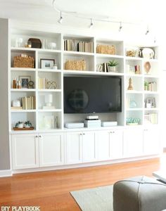 a living room with white bookcases and a flat screen tv on the wall