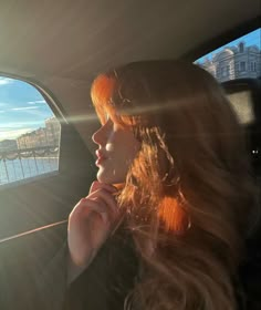 a woman sitting in the back seat of a car looking out at water and buildings