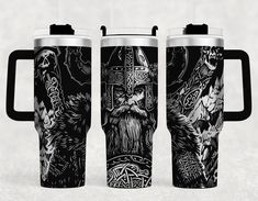 three black and white travel mugs with designs on the sides, one has a viking head