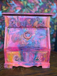 an old dresser painted pink and blue with colorful flowers on it's sides, sitting on a wooden table