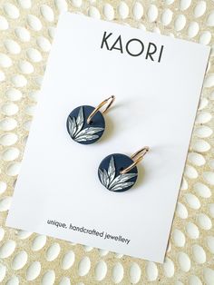 a pair of earrings sitting on top of a white table next to an advertisement for kaori