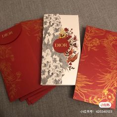 three red envelopes are sitting next to each other on a gray surface with the word dior printed on it