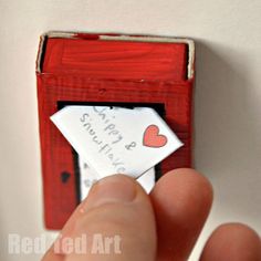 someone is holding a piece of paper in front of a red box with a heart on it