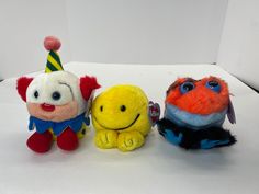 three stuffed animals sitting next to each other on a white surface with one being a clown