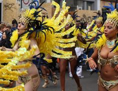 two women in yellow and blue costumes are dancing on the street with other people watching